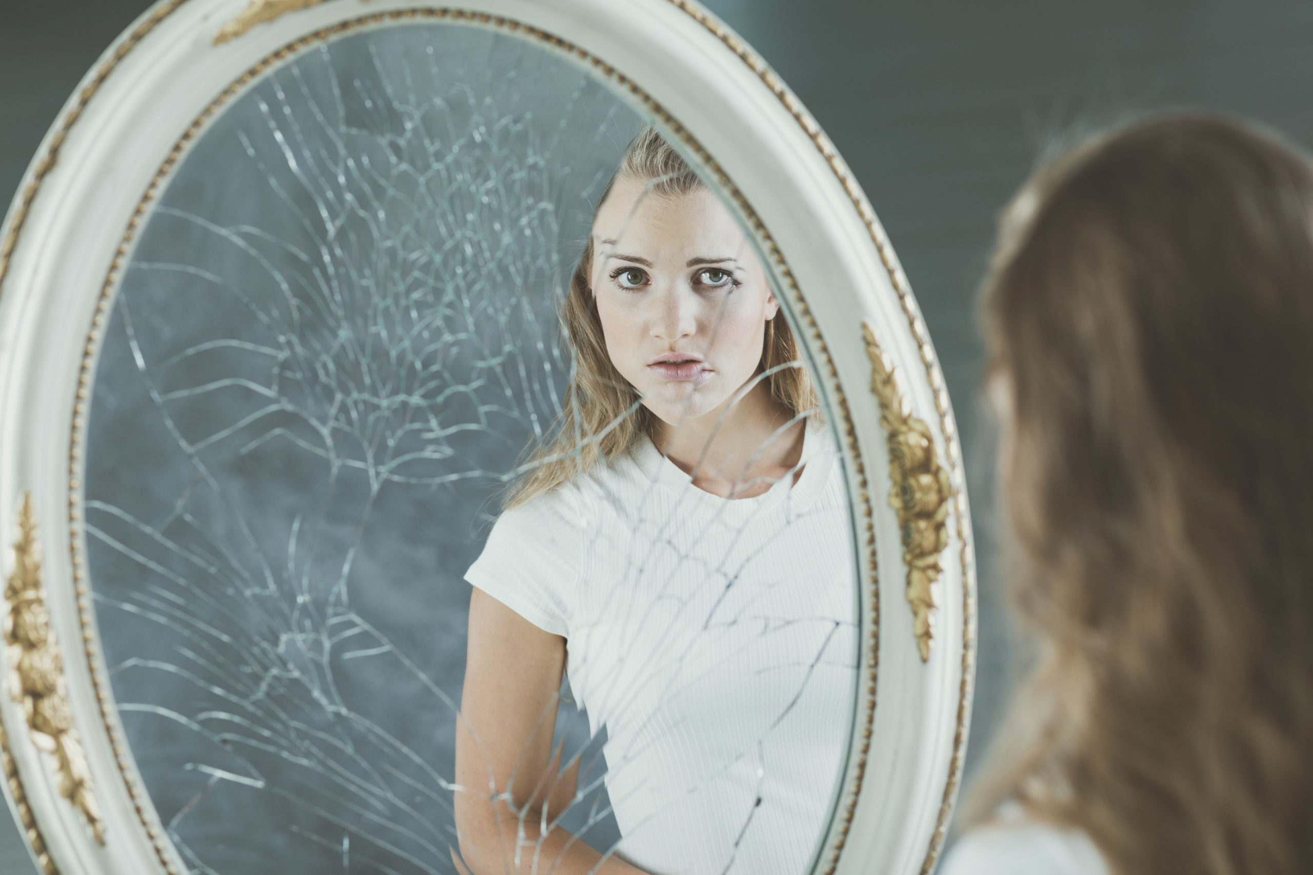 Pretty teenage girl with personality problems looking at herself in the mirror
